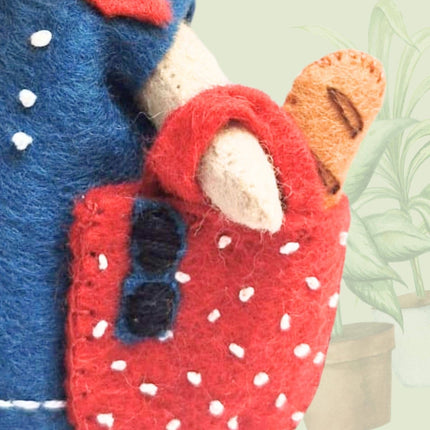 Close-up of a red felted product with white spots, blue accents, and a green plant in the background.
