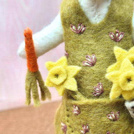 Felted toy with a green dress and yellow flowers on a pink background