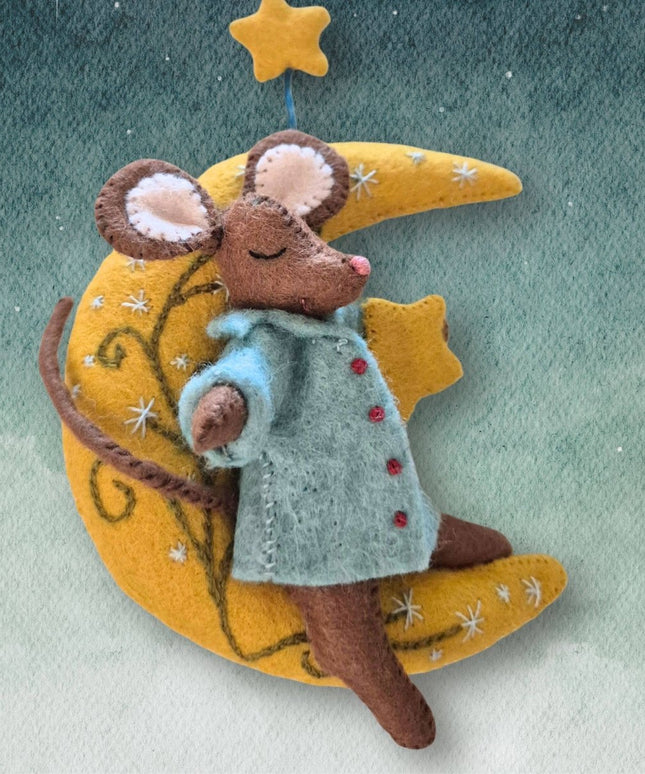 A felt mouse wearing a light blue coat with red buttons, resting on a yellow crescent moon and star decoration against a soft green-blue textured background.