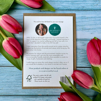 Card with text and a logo surrounded by pink tulips on a wooden surface