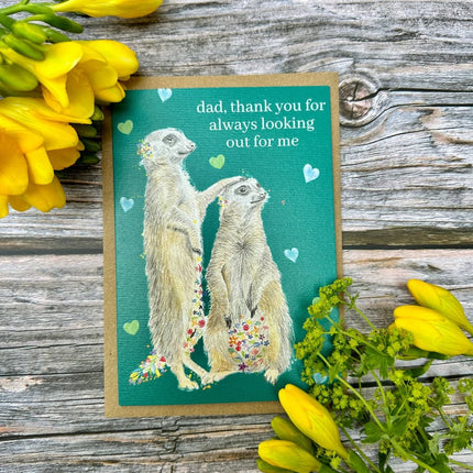 Greeting card with meerkats and flowers on a wooden surface