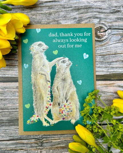 Greeting card with meerkats and flowers on a wooden surface