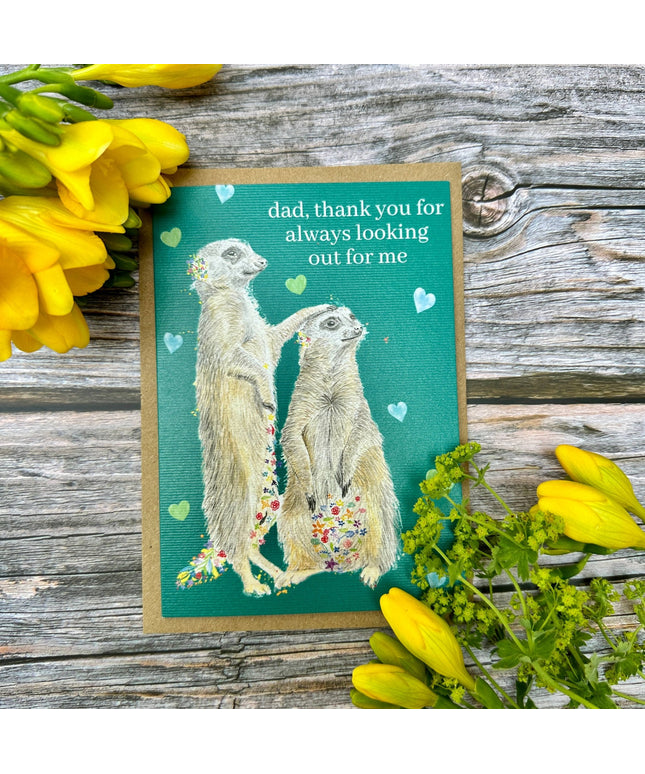 Greeting card with meerkats and flowers on a wooden surface