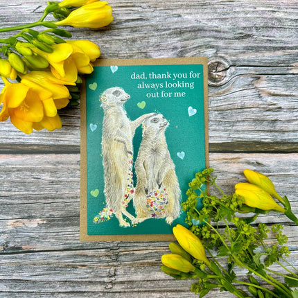 Card with meerkats and flowers on a wooden surface
