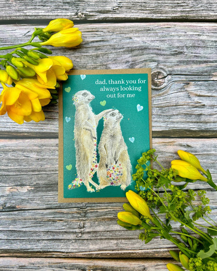 Card with meerkats and flowers on a wooden surface