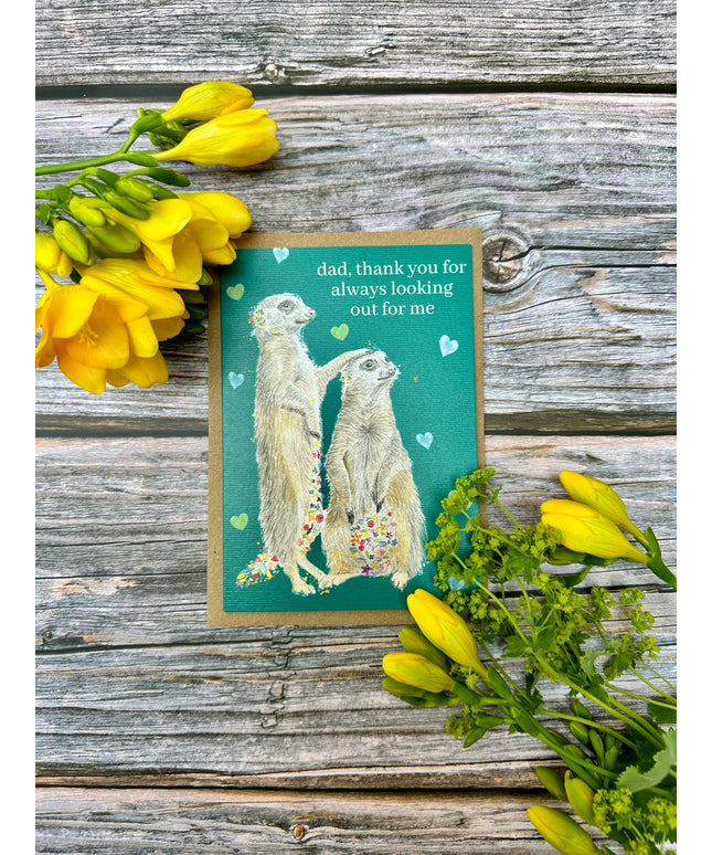 Card with meerkats and flowers on a wooden surface