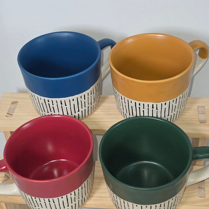 Four ceramic mugs in mustard yellow, dark green, blue, and red