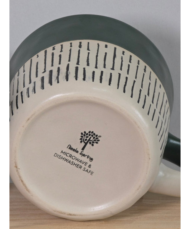 Close-up of the bottom of a ceramic mug or pitcher, showing a cream-colored base with black printed text that reads Microwave & Dishwasher Safe' alongside a tree logo. 