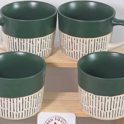 Four ceramic mugs with dark green interiors and handles, paired with cream-colored exteriors featuring a black dash pattern.