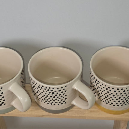 Three ceramic mugs with a black dotted pattern on the exterior and a warm cream interior.