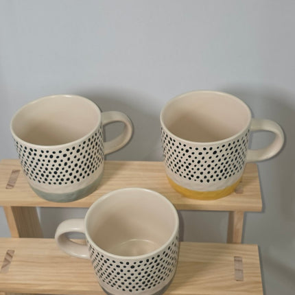 Three ceramic mugs with a black dotted pattern on the exterior and cream-colored interiors