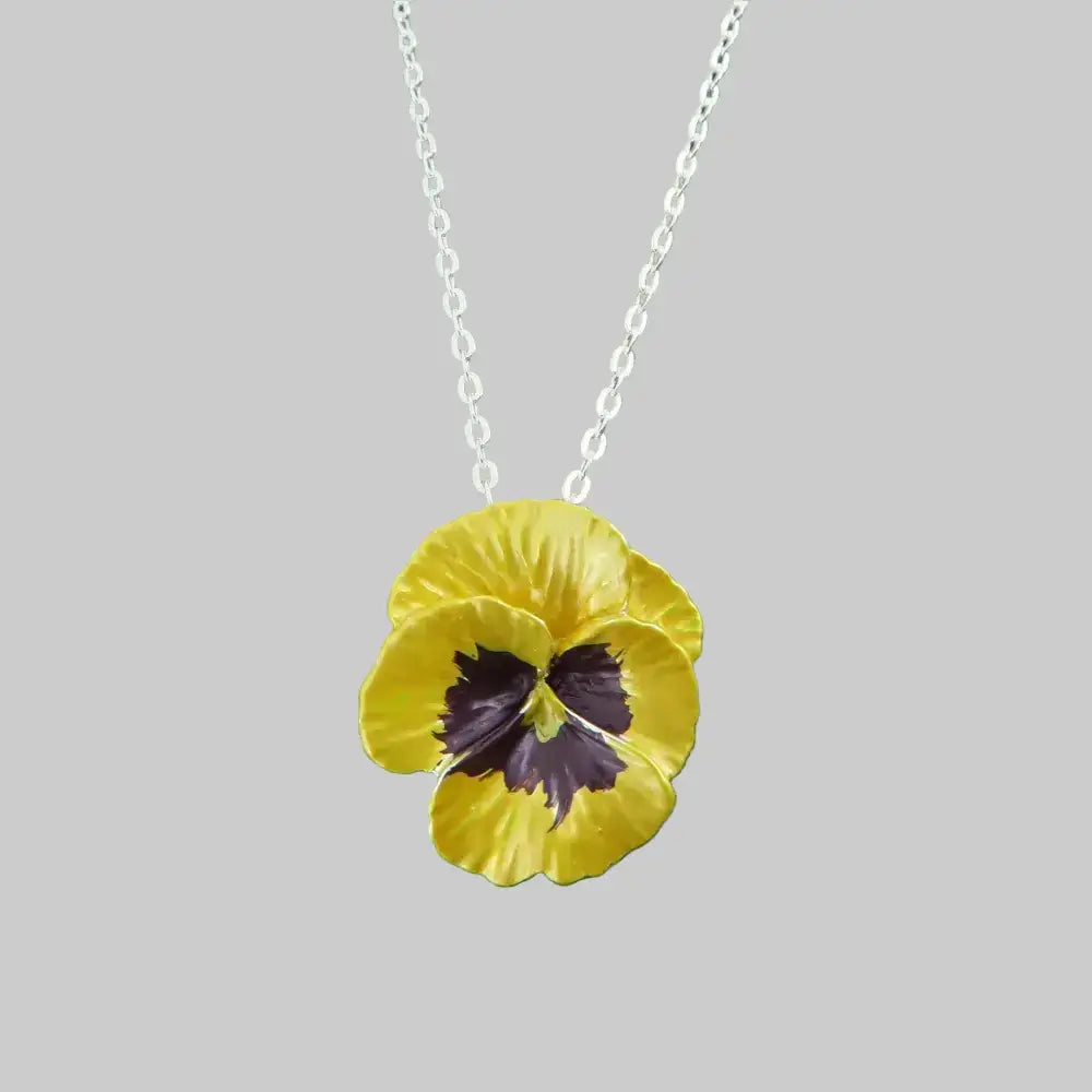 Yellow pansy flower pendant on a silver chain against a gray stone background