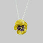 Yellow pansy flower pendant on a silver chain against a gray stone background