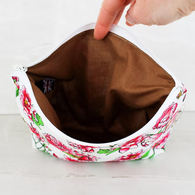 Floral-patterned fabric pouch with a brown interior, held open by a hand on a white background.