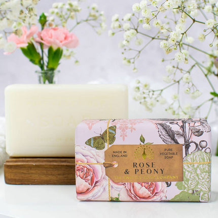 Bar of soap with a decorative box labeled 'Rose & Peony' on a white surface with flowers in the background.