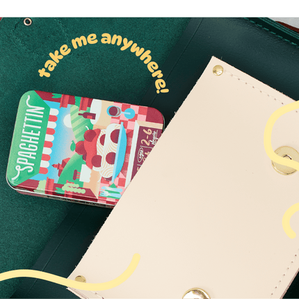 A close-up of a dark green leather wallet or clutch with a cream-colored snap flap, showing a small colorful 'Spaghetti' card tucked inside. Yellow decorative script text reads 'take me anywhere!' and wavy lines overlay the photo.